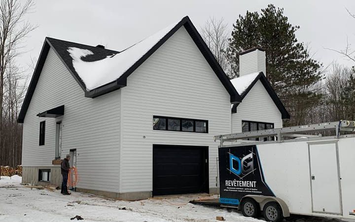 Une maison blanche avec un toit noir et une caravane garée devant.