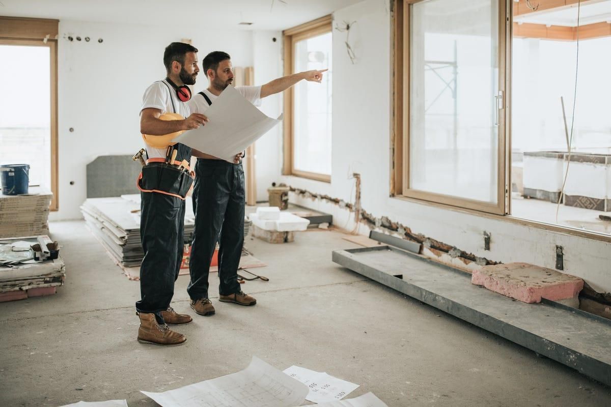 Two men are standing in a room looking at a blueprint.