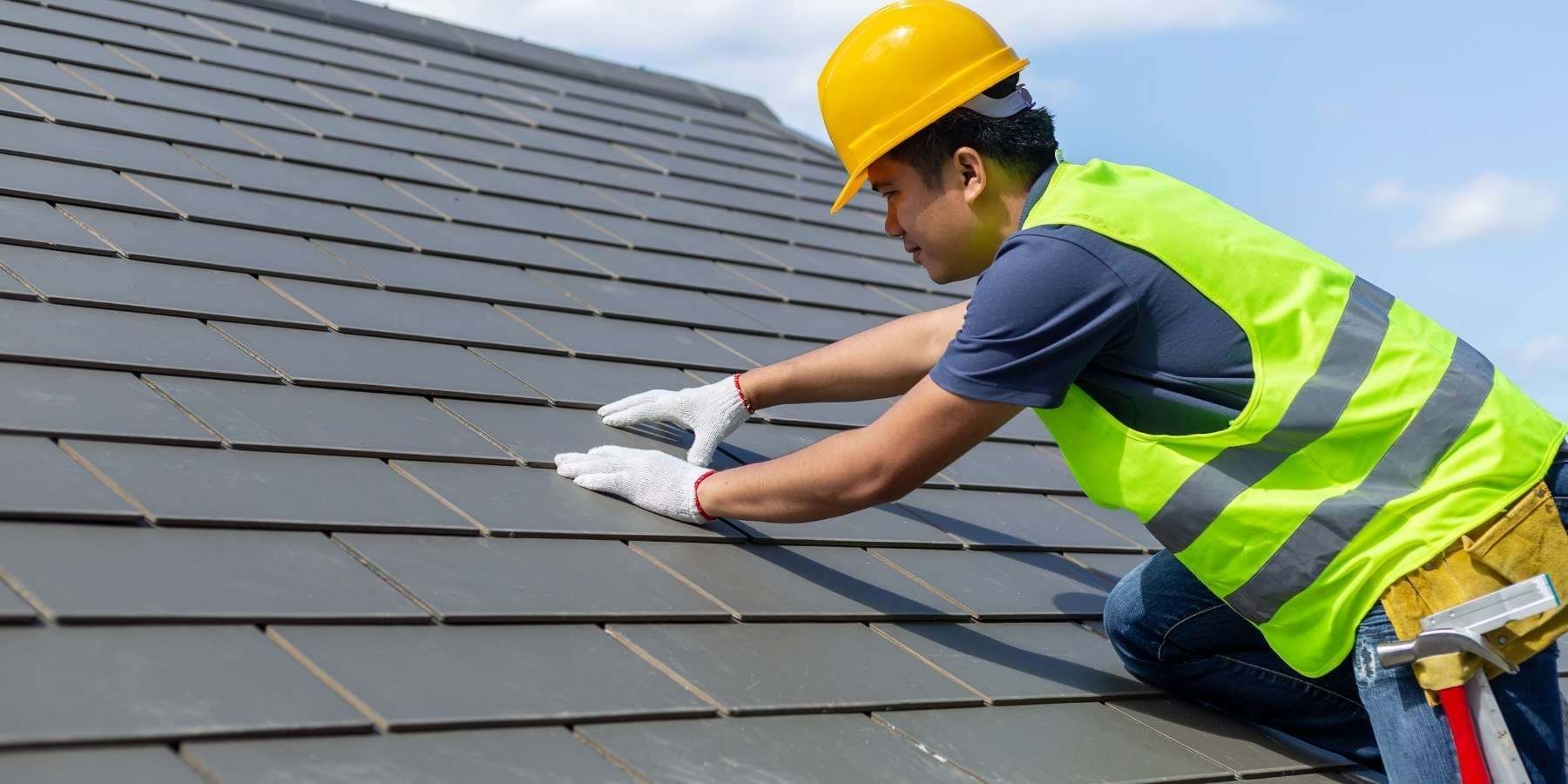 A man wearing a hard hat and safety vest is working on a roof.