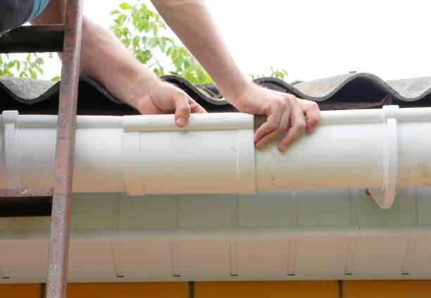 A person is fixing a gutter on the roof of a house.