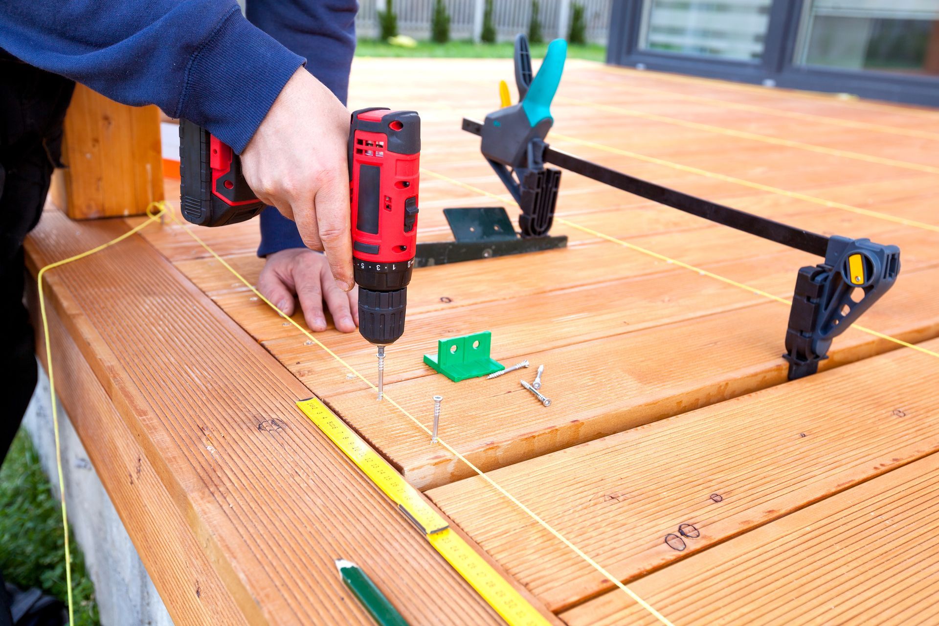A person is using a drill on a wooden deck.