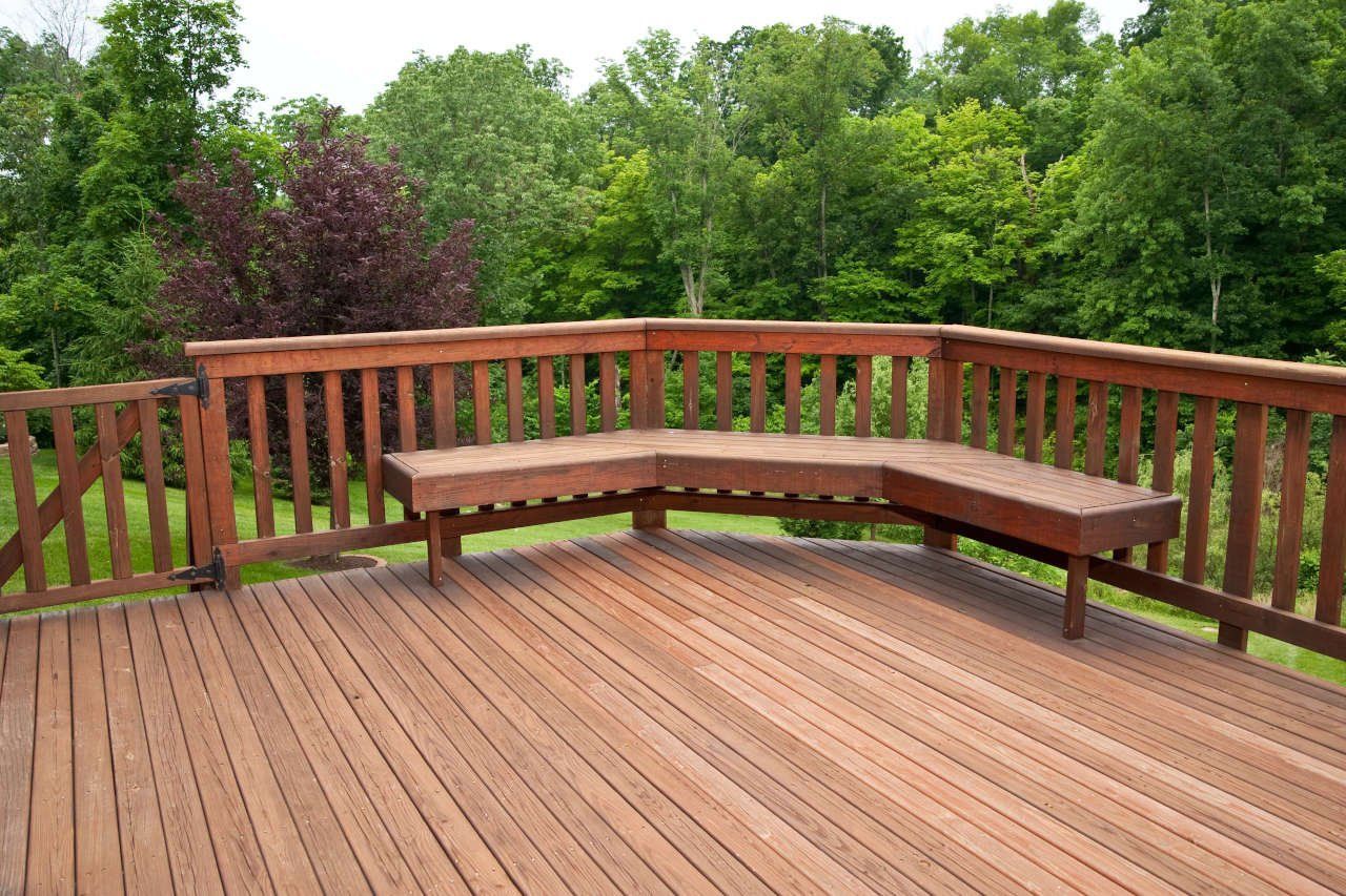 A wooden deck with a curved bench and trees in the background