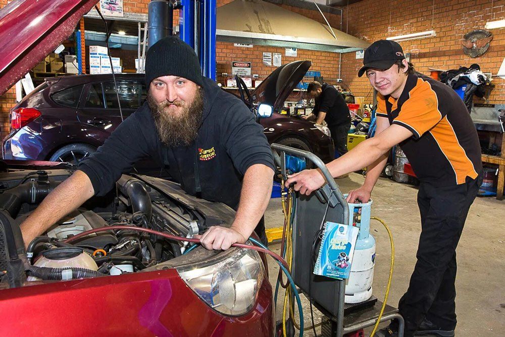 Two Automotive Worker Smiling On Camera While Fixing The Red Car On The Shop — Golf Carts and Auto Electrical Services in Orange
