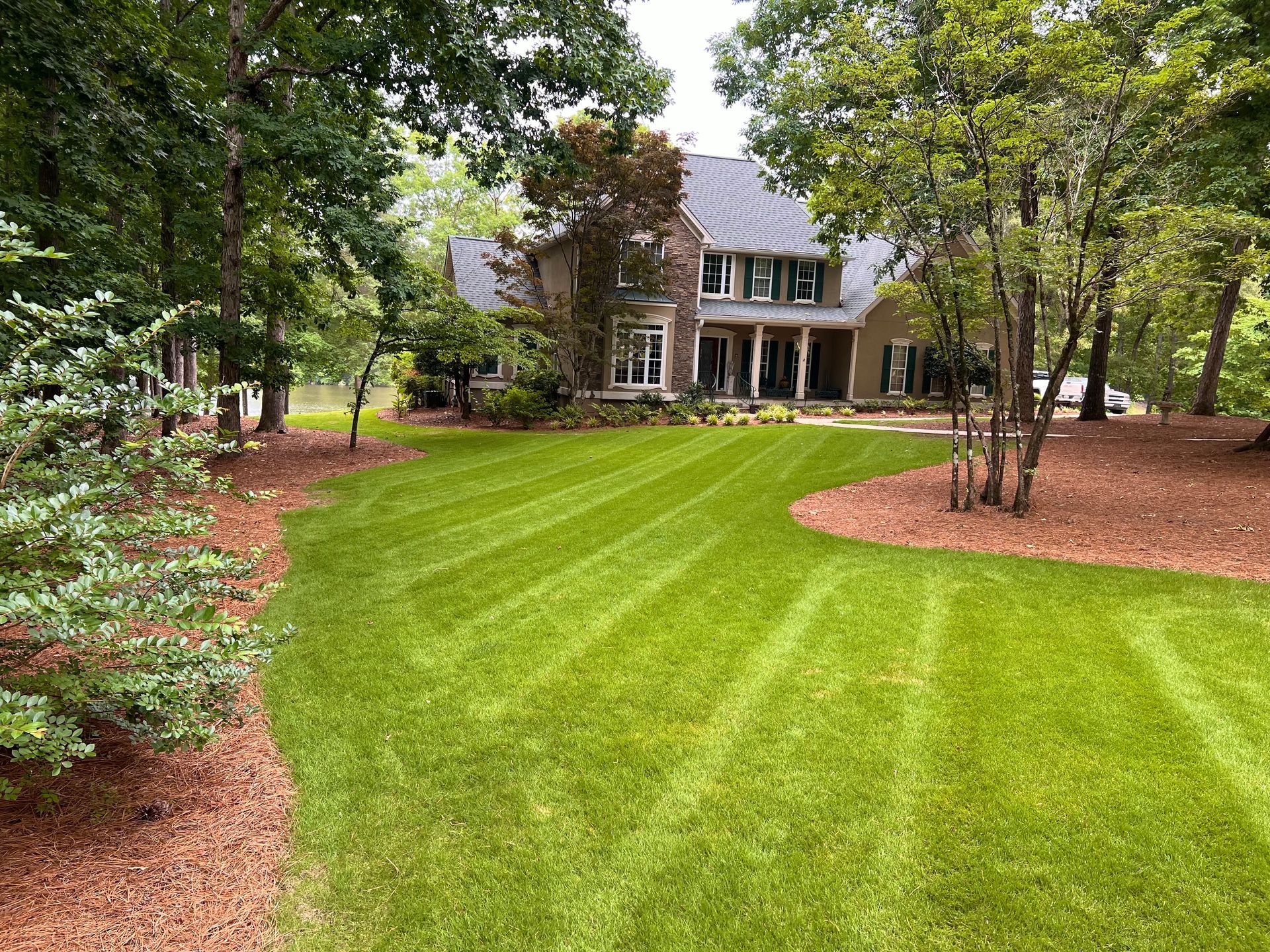 A large house with a lush green lawn in front of it surrounded by trees.