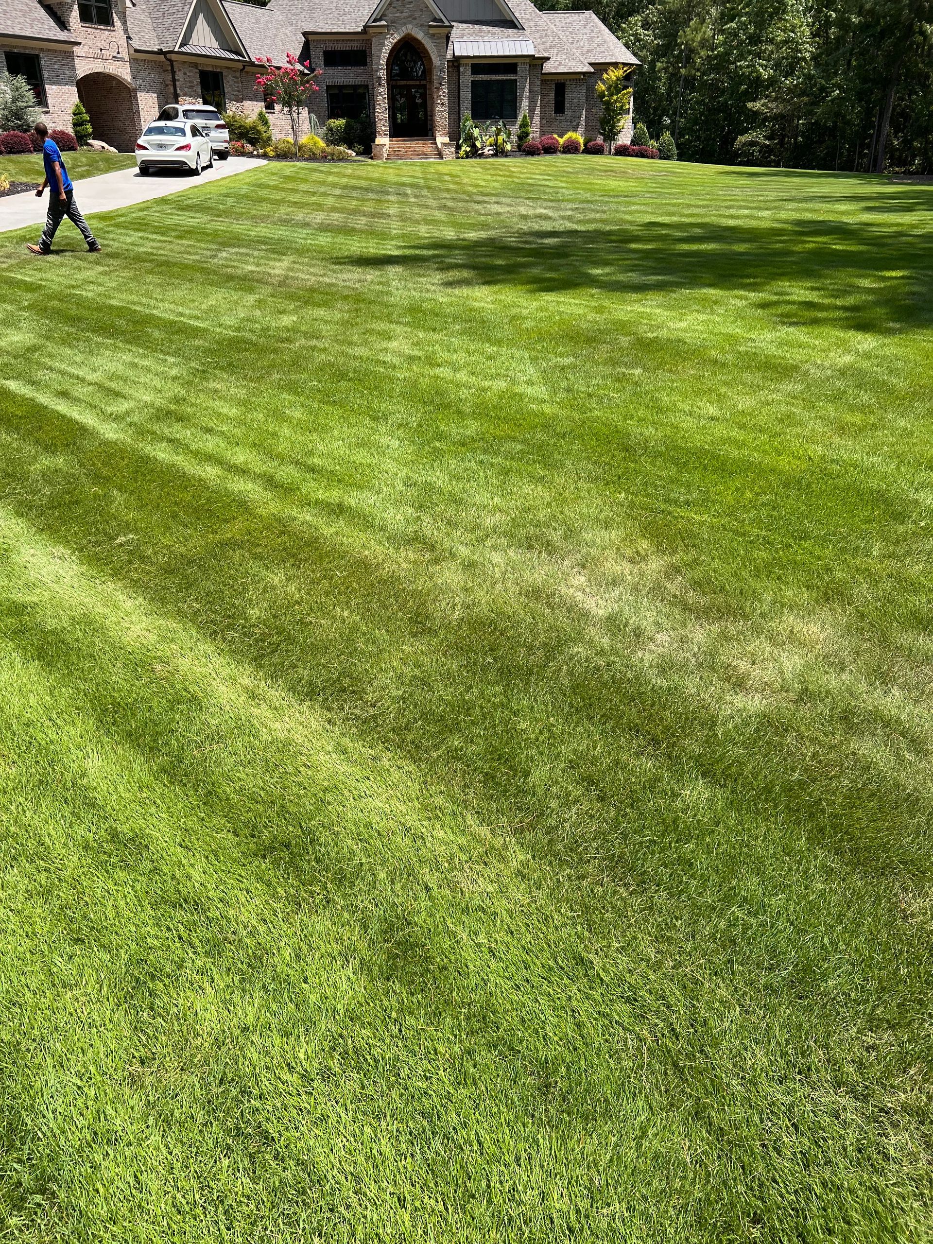 A man is mowing a lush green lawn in front of a large house.
