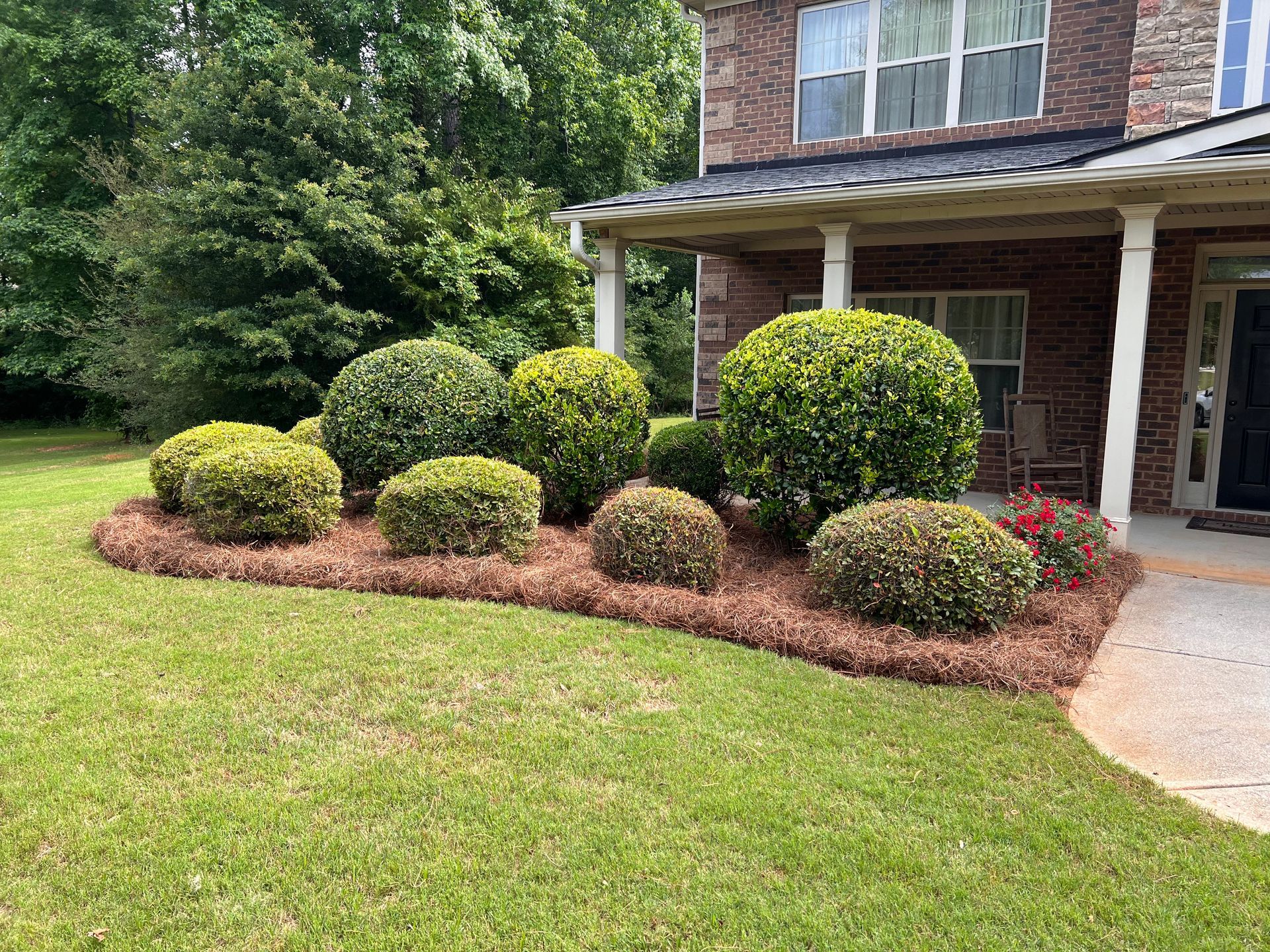 A brick house with a lush green lawn and bushes in front of it.