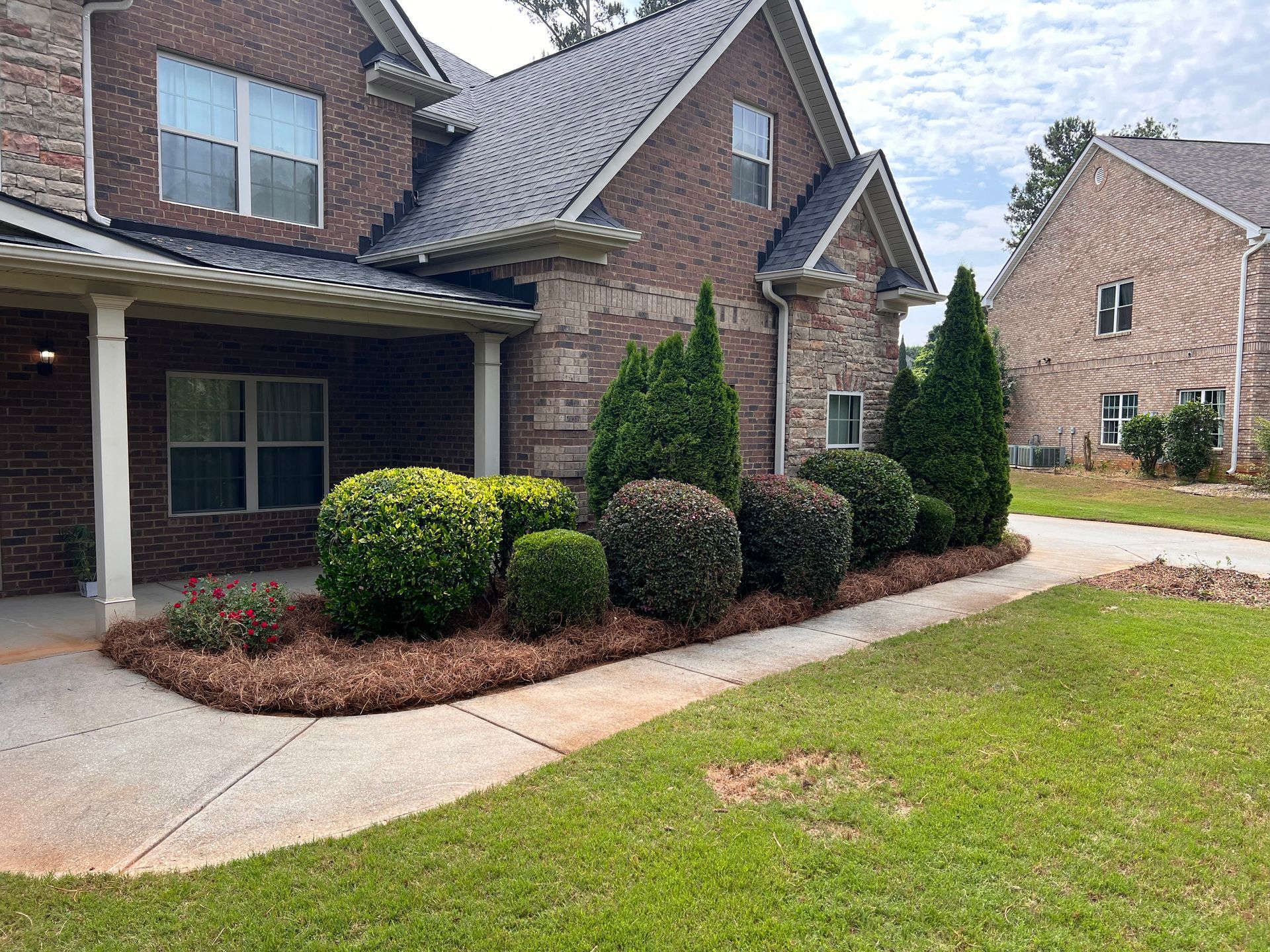 A brick house with a lush green lawn and bushes in front of it.