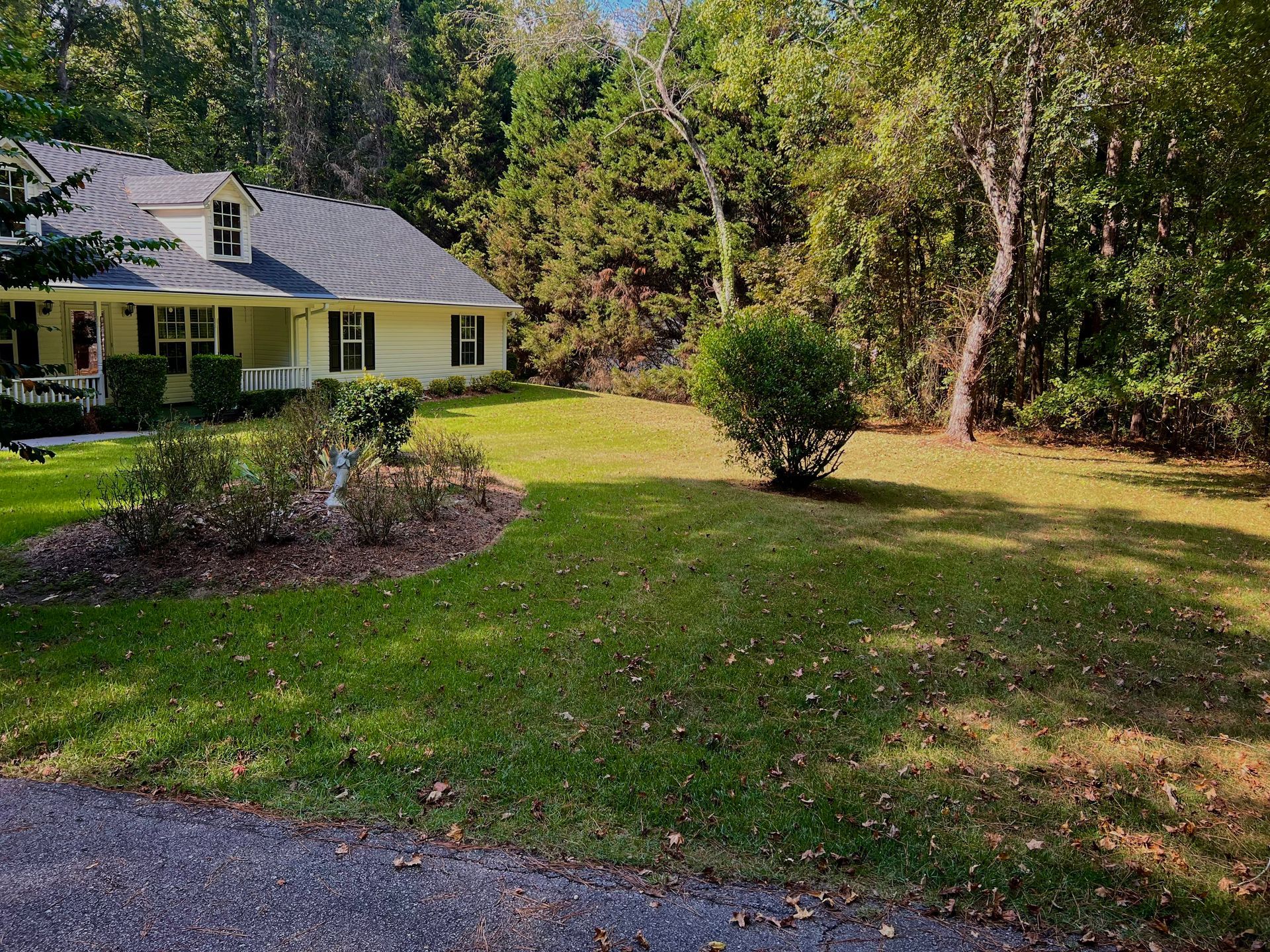 A white house with a gray roof is surrounded by trees and grass.