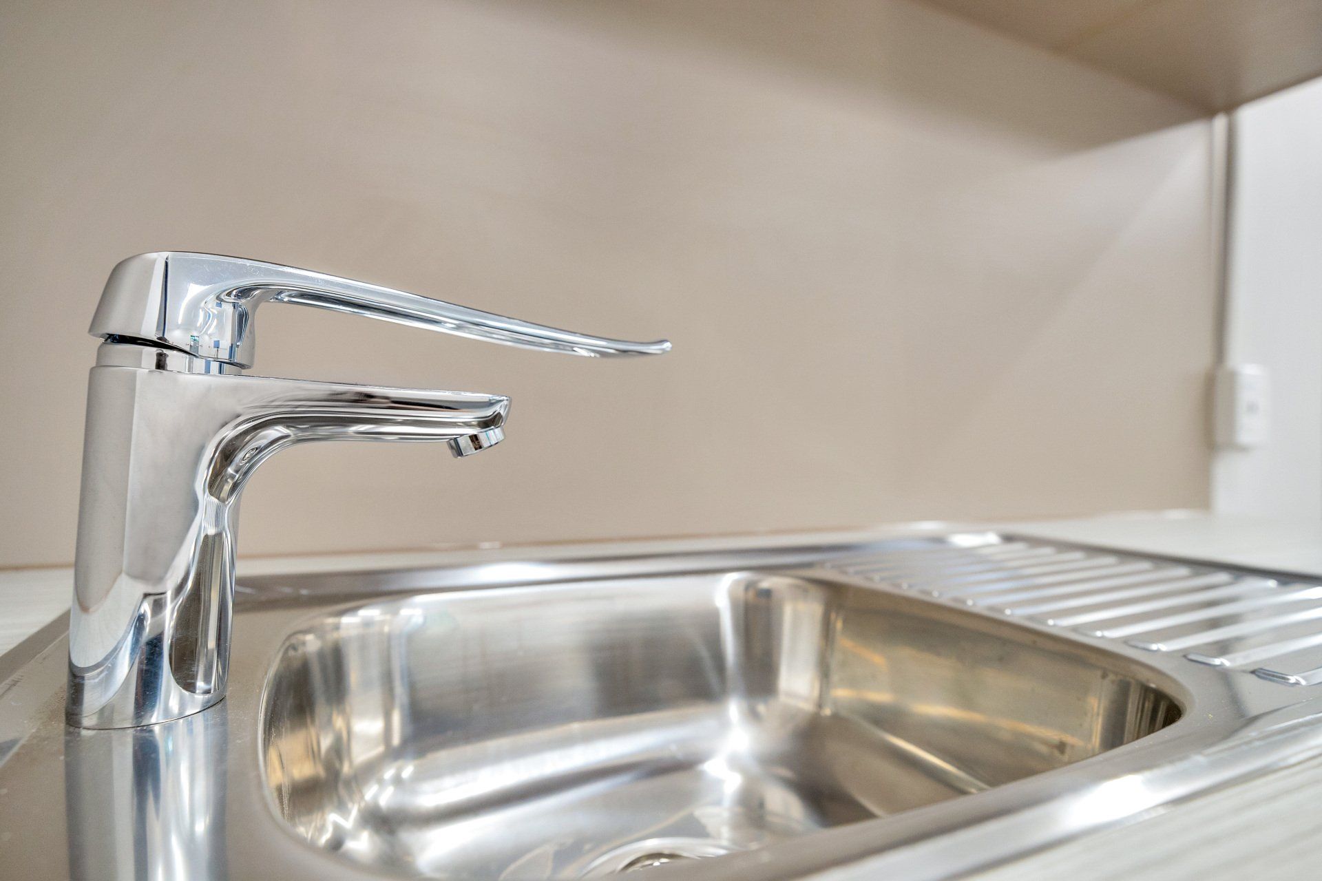 Chrome faucet over a stainless steel sink, indoors, neutral background.