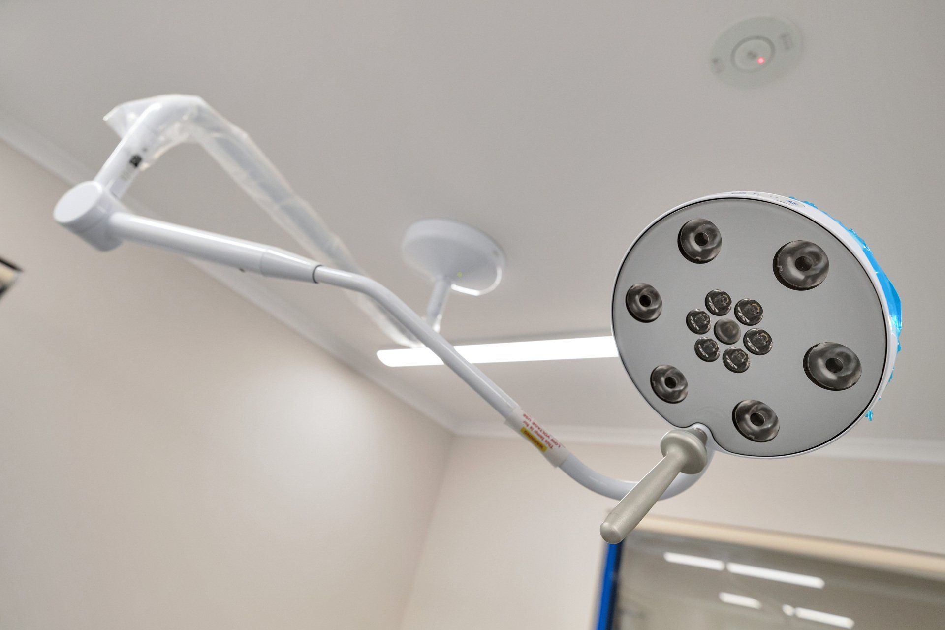 Surgical overhead lamp, white and blue, in a room with white walls and a window.