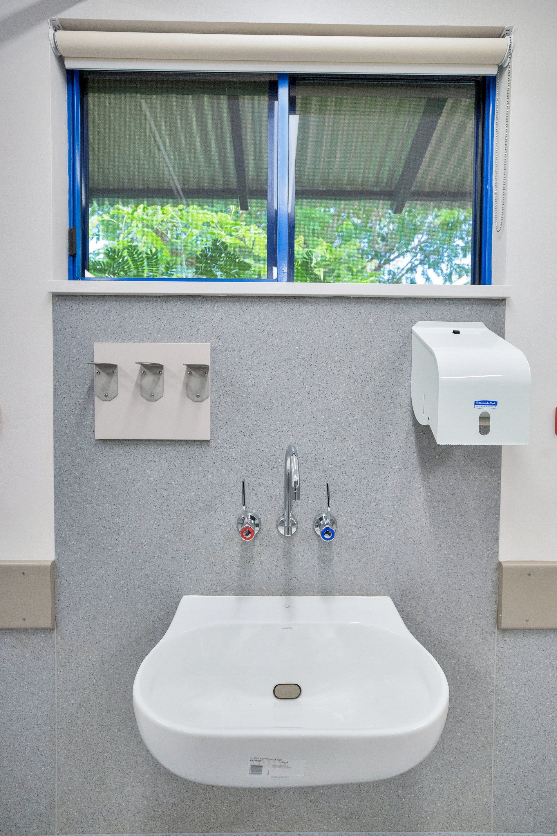 Bathroom sink with red/blue faucets, dispenser, and window.