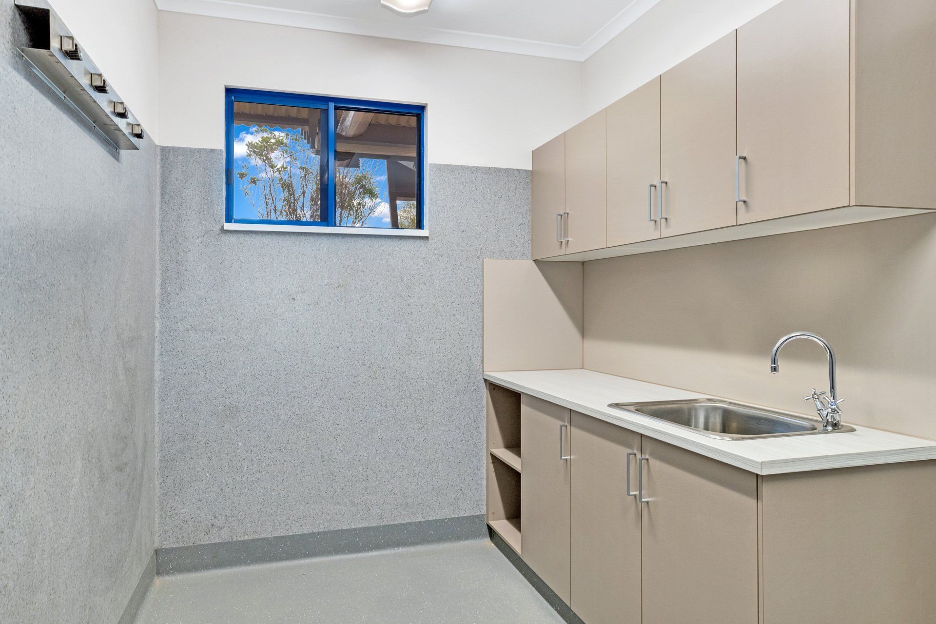 Laundry room with light brown cabinets, a stainless steel sink, and a blue window. Gray walls.