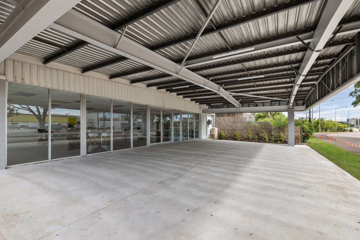 Exterior view of a building with a covered patio and glass windows. Concrete ground, gray roof.