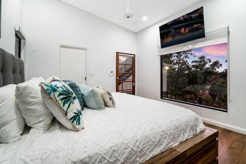Bedroom with white bed, view of trees through window, TV above the window.