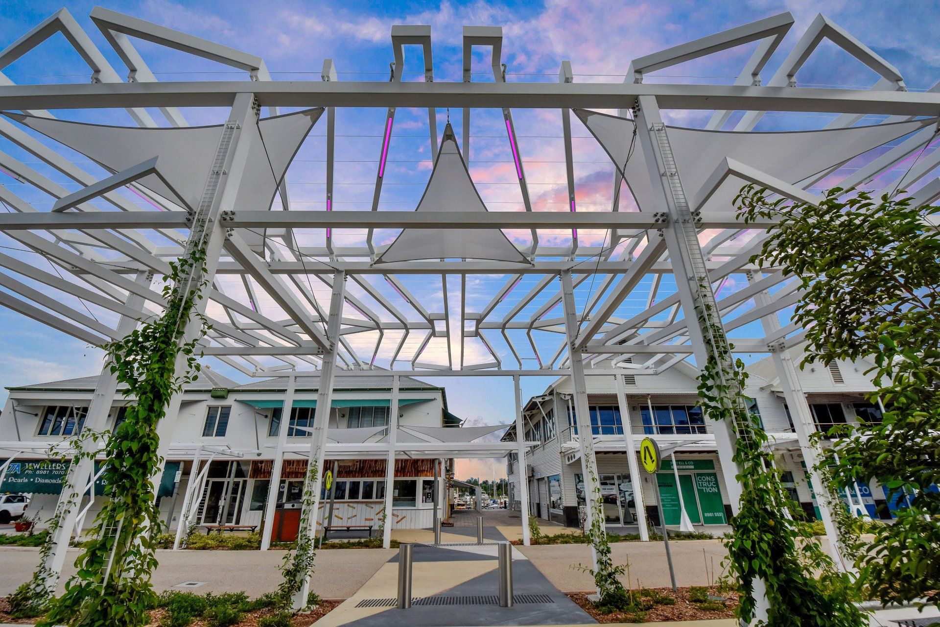 White pergola over shops with trailing green vines, blue sky.