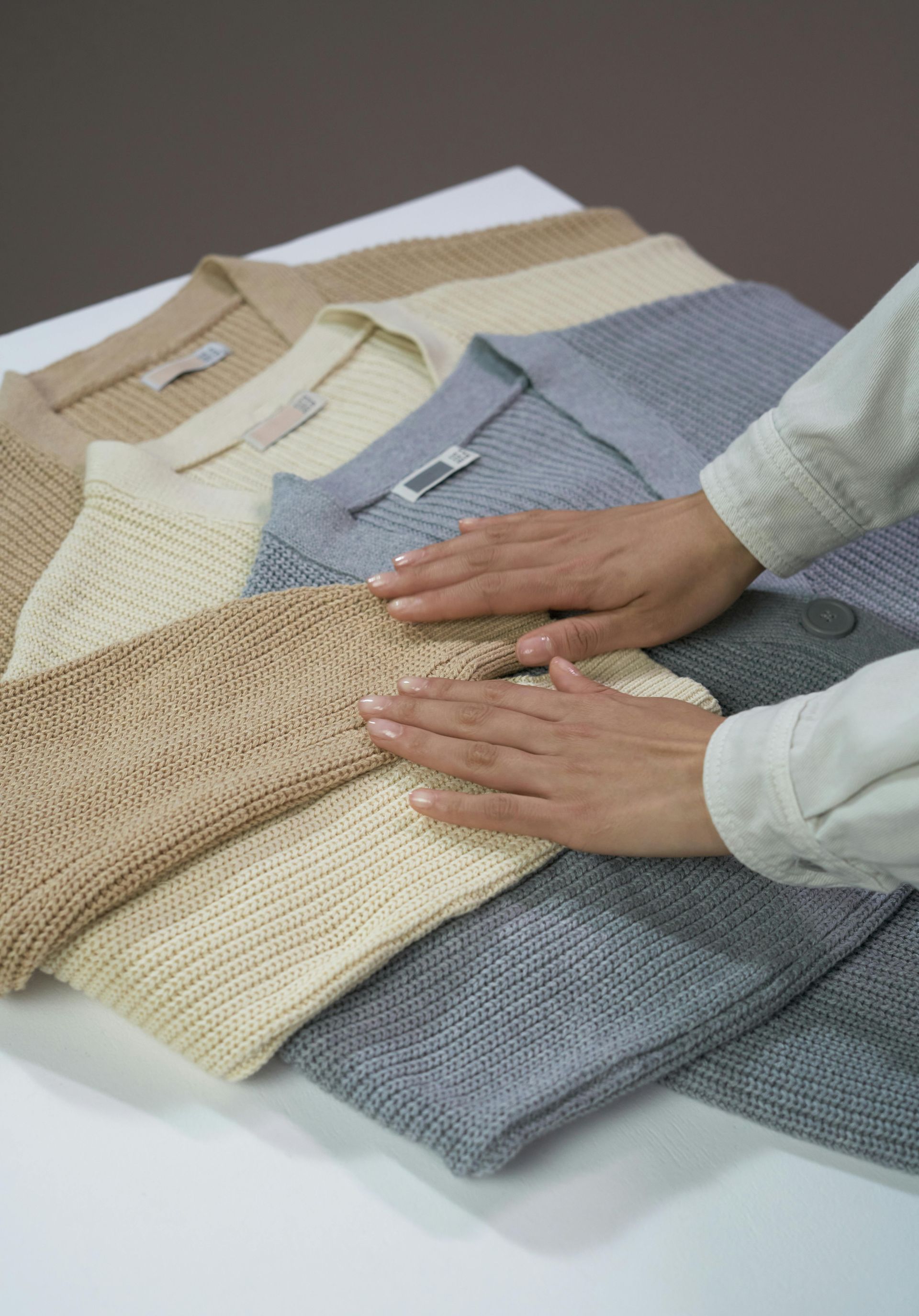 A person is touching a pile of sweaters on a table.