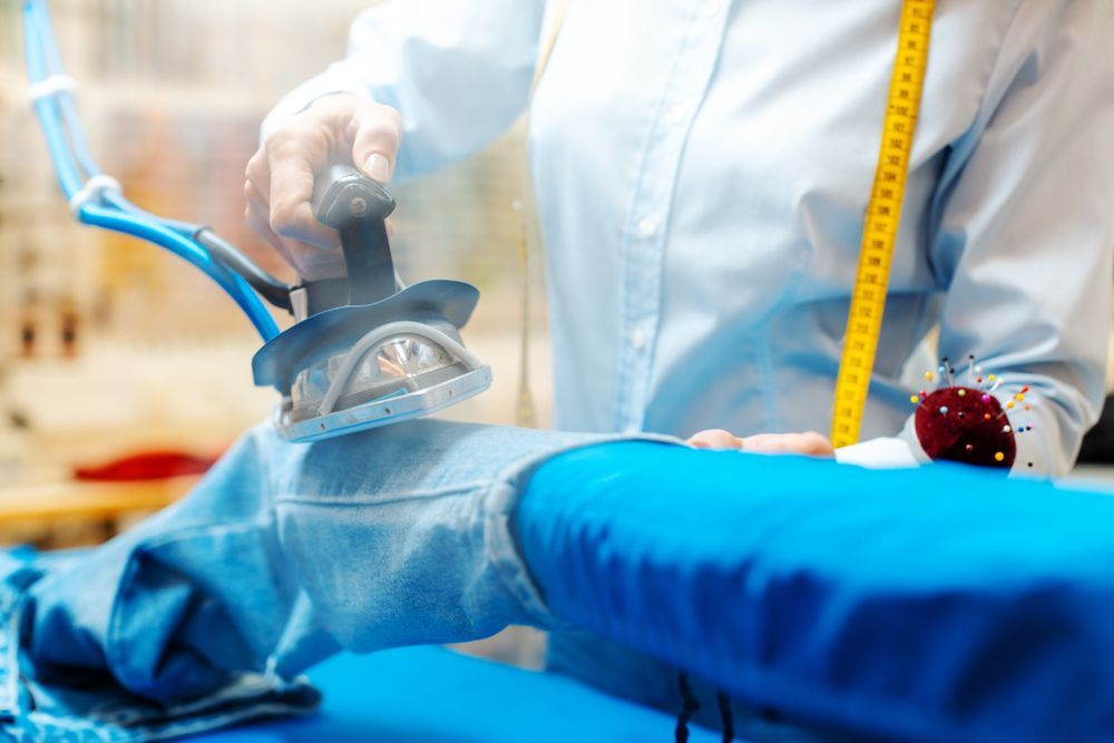 A person is ironing a pair of jeans on a blue ironing board.