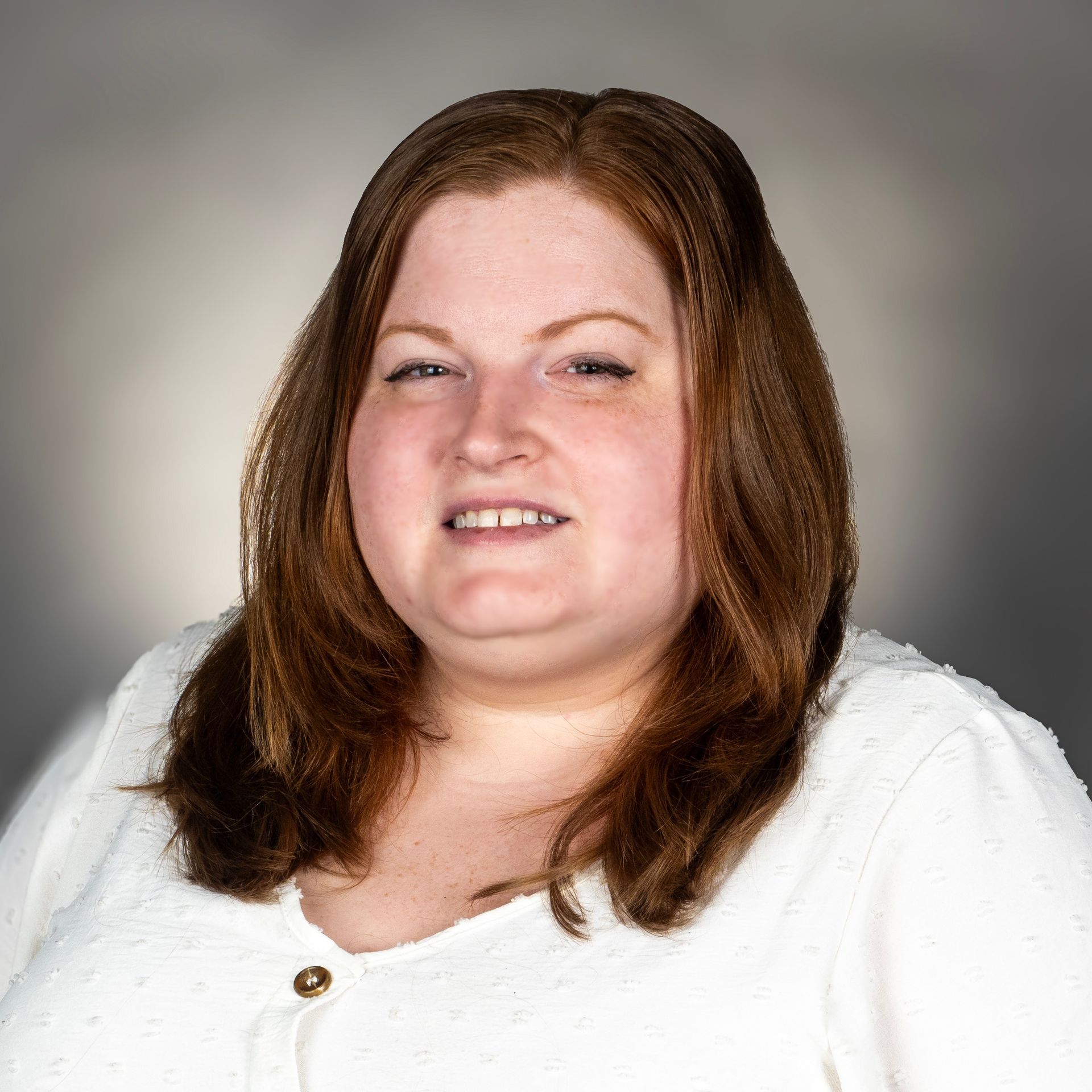 A woman with red hair and a white shirt smiles at the camera. She is set against a gray backdrop.