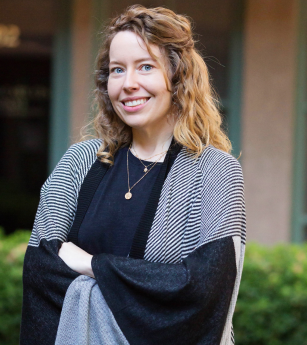 A woman wearing a black shirt and a striped cardigan is smiling for the camera.