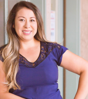 A woman in a blue shirt is smiling and standing with her hands on her hips.