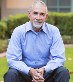 A man in a blue shirt sits with his hands folded
