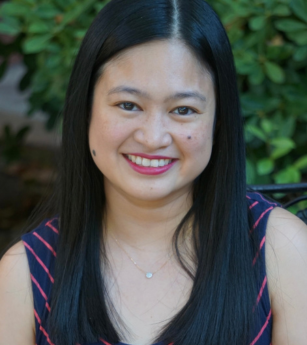 A woman with long black hair is smiling for the camera while sitting on a bench.