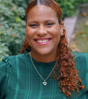 A woman wearing a green shirt and a necklace is smiling.