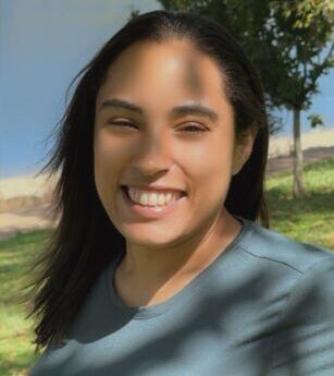 A woman in a blue shirt is smiling in a park.
