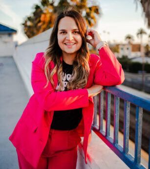 A woman in a pink suit is leaning on a railing and smiling.