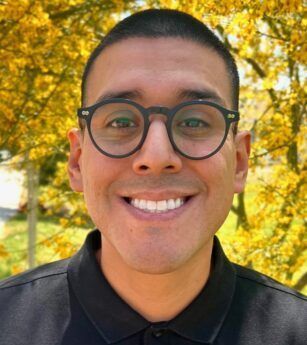 A man wearing glasses and a black shirt is smiling for the camera.