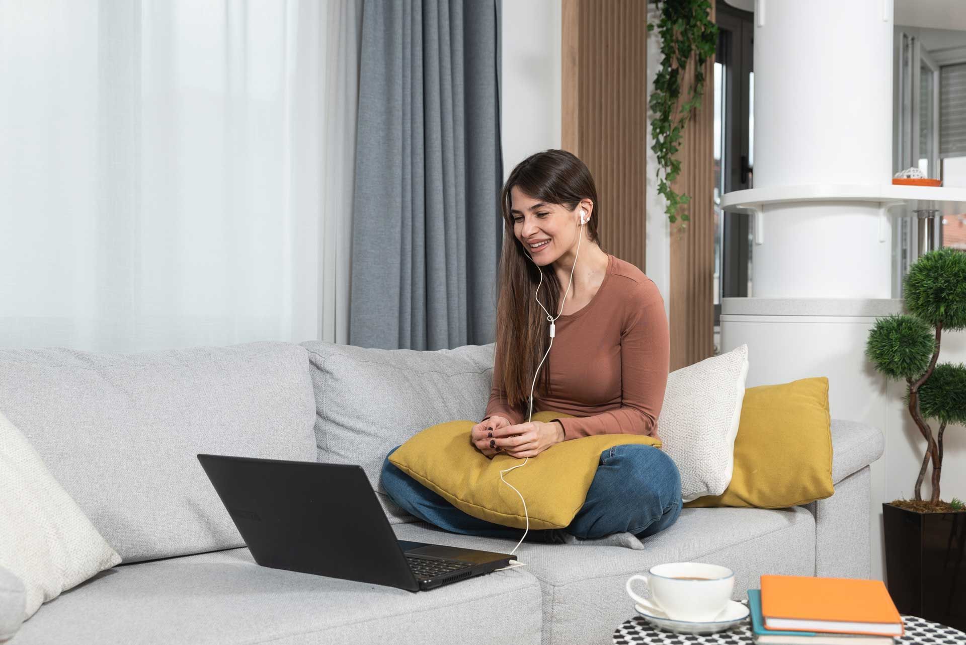 A woman is sitting on a couch using a laptop computer.