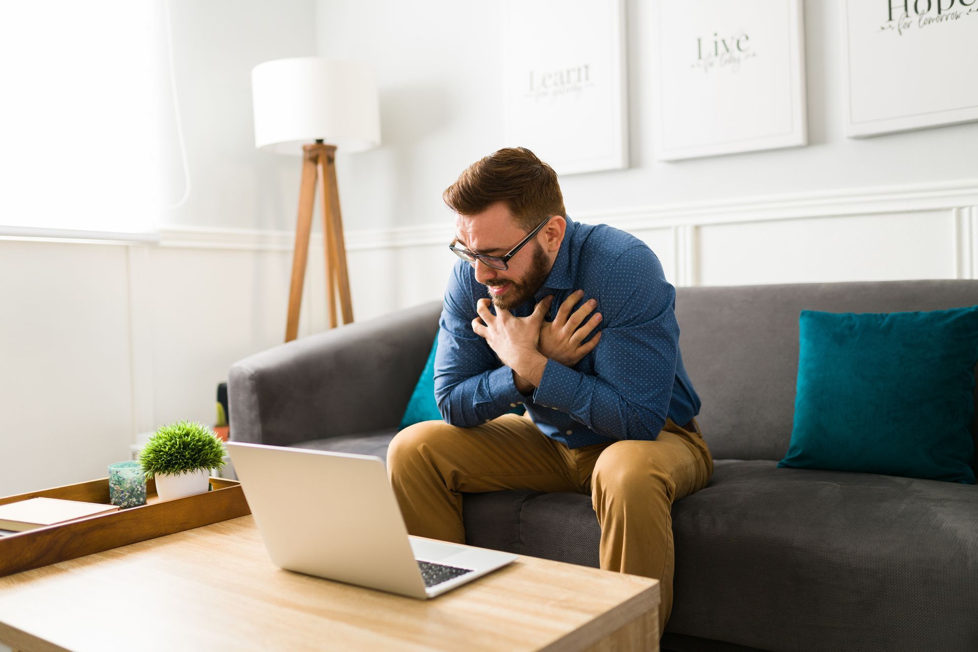 A man is sitting on a couch in front of a laptop computer.