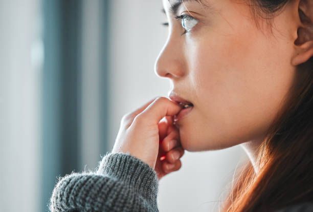 A woman is biting her nails while looking out of a window.