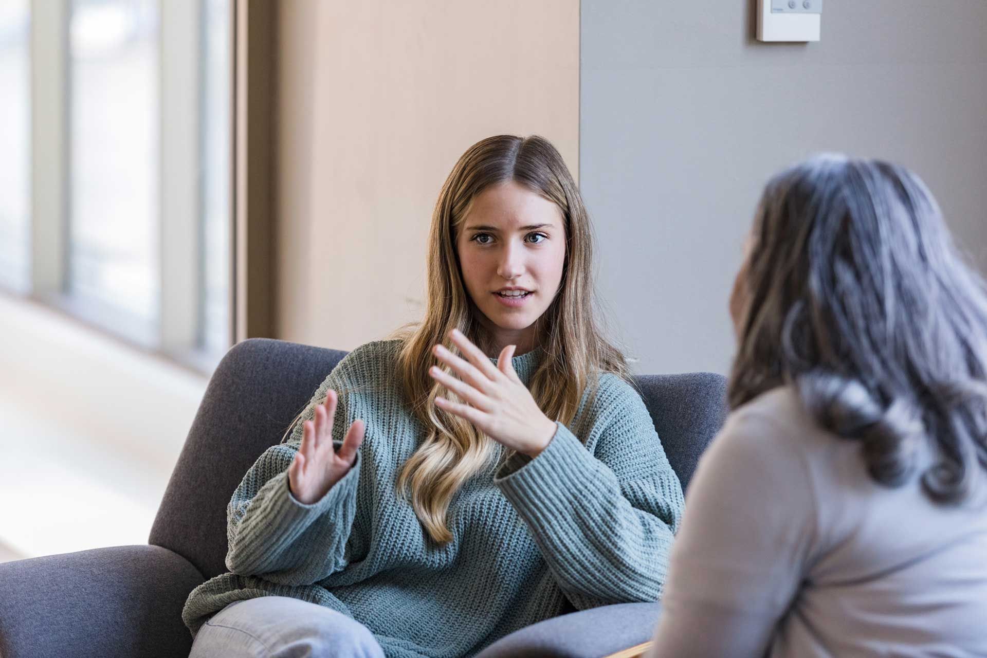 A woman is sitting on a couch talking to another woman.