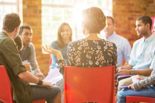 A woman is sitting in a red chair talking to a group of people.