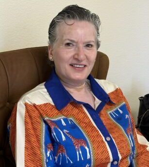 A woman is sitting in a chair wearing an orange and blue shirt with giraffes on it