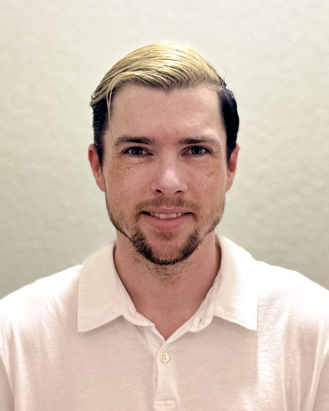 A man with a beard is wearing a white shirt and smiling for the camera.