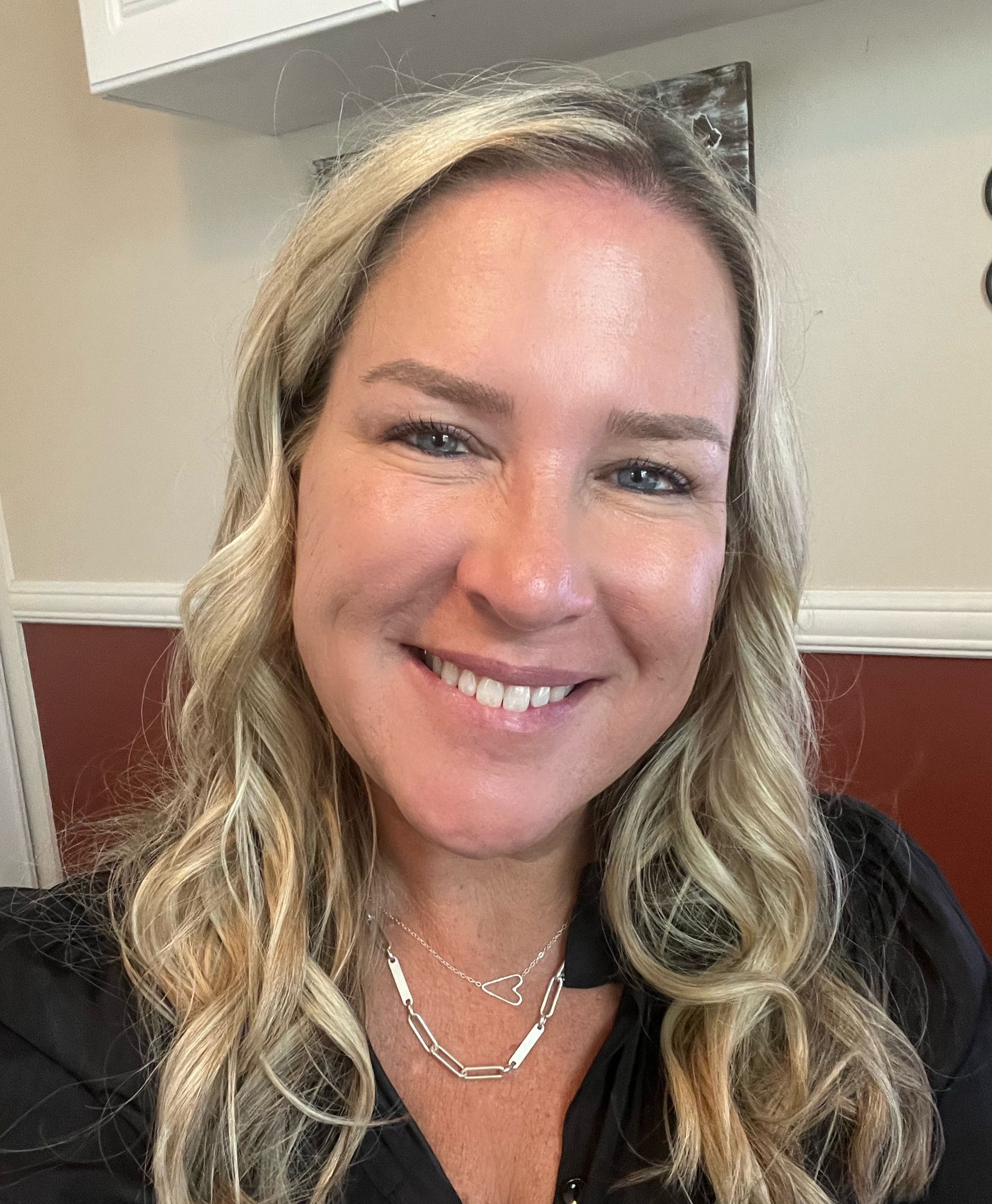 A woman with long blonde hair and a necklace is smiling for the camera.