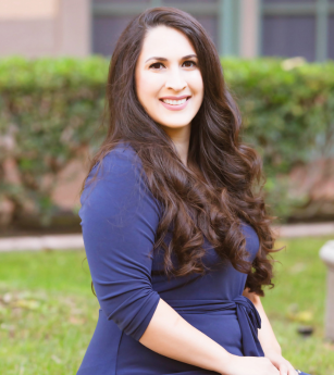 A woman in a blue dress is sitting in the grass and smiling.