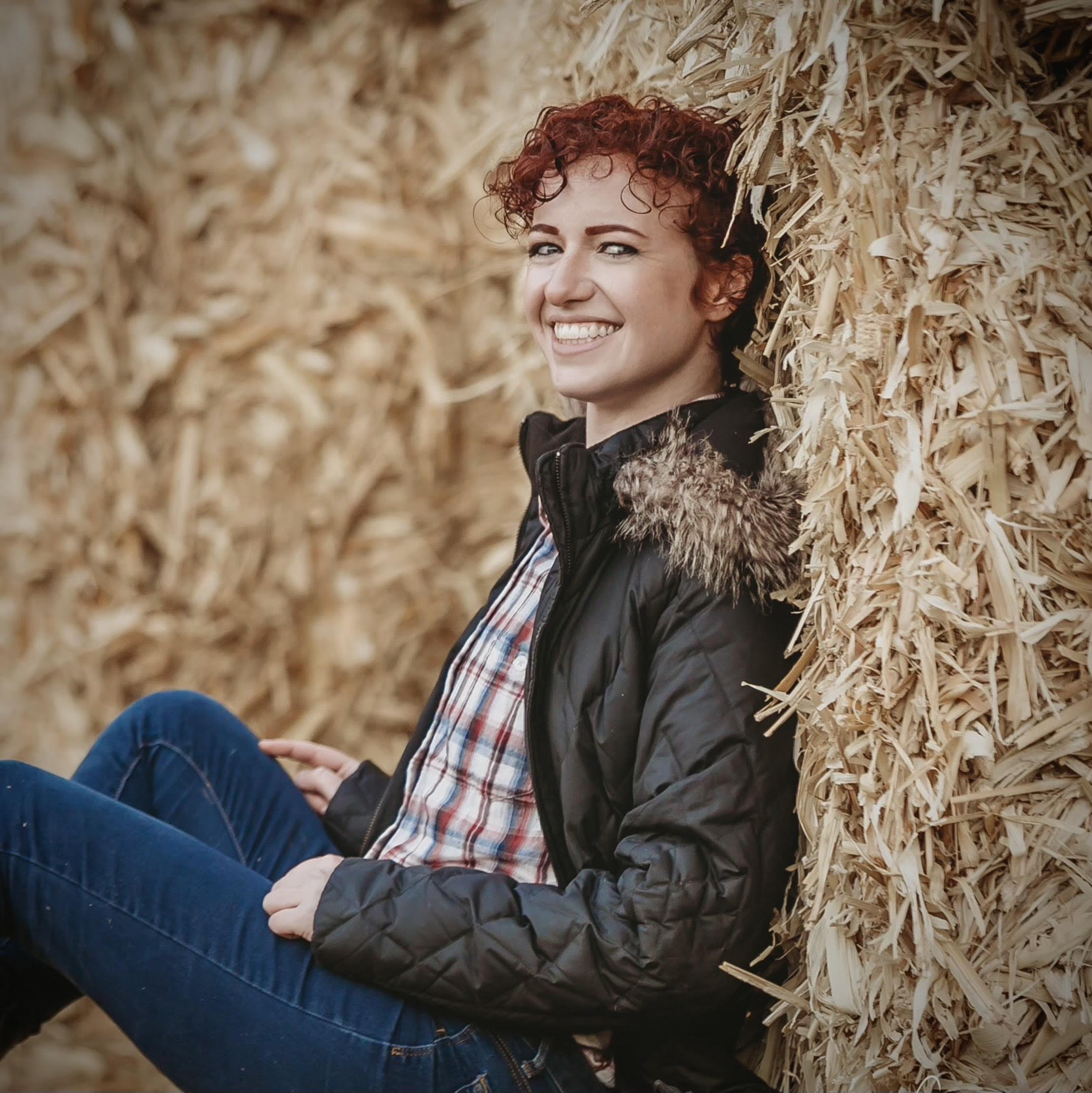 A woman leaning against a pile of hay and smiling