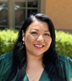 A woman in a green shirt is smiling for the camera.