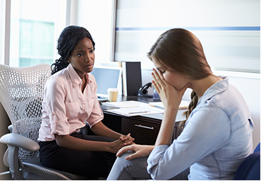 A woman is sitting at a desk talking to another woman.