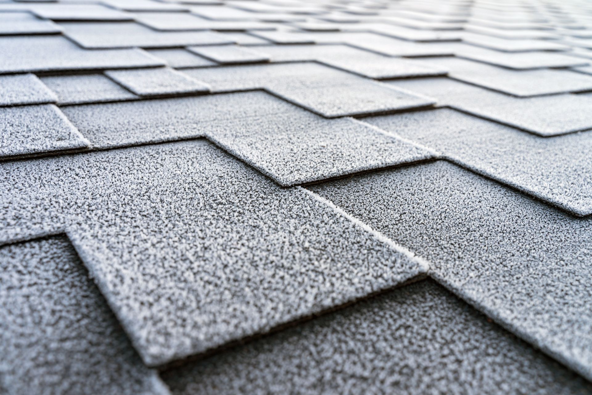 Close-up of gray asphalt roof shingles covered in frost.