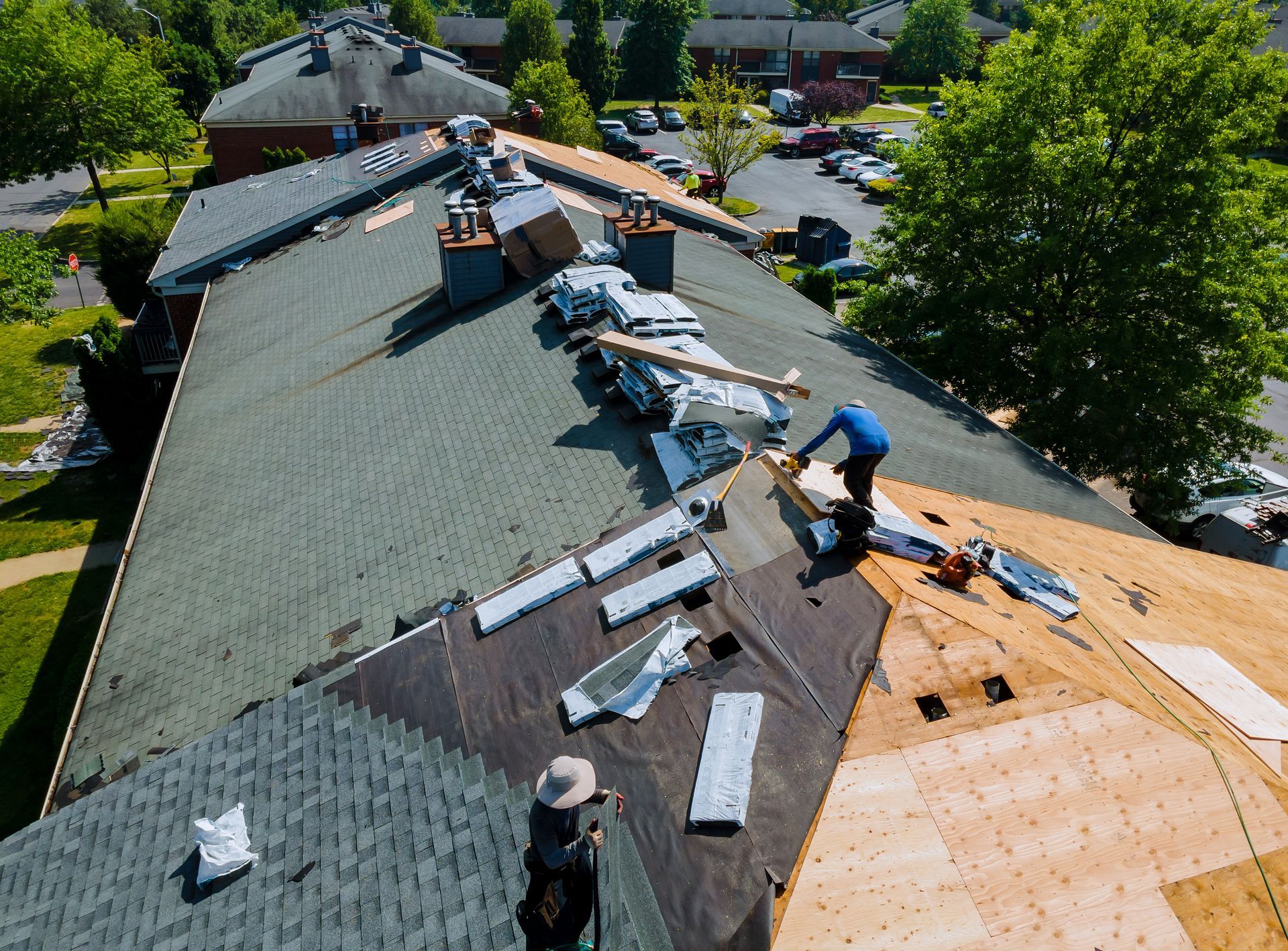 Roofers replacing shingles on a building; some shingle sections removed, others covered. Sunny day.