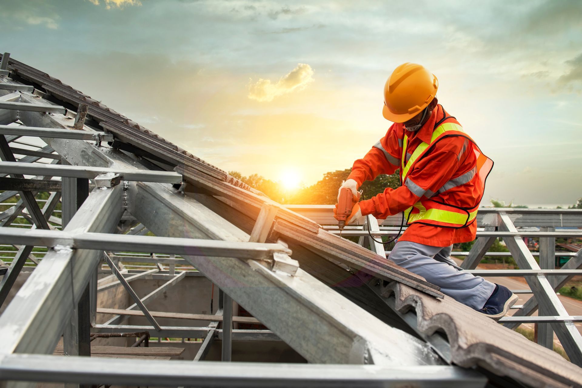 Construction worker in orange safety gear installing roof tiles on a sunny day.
