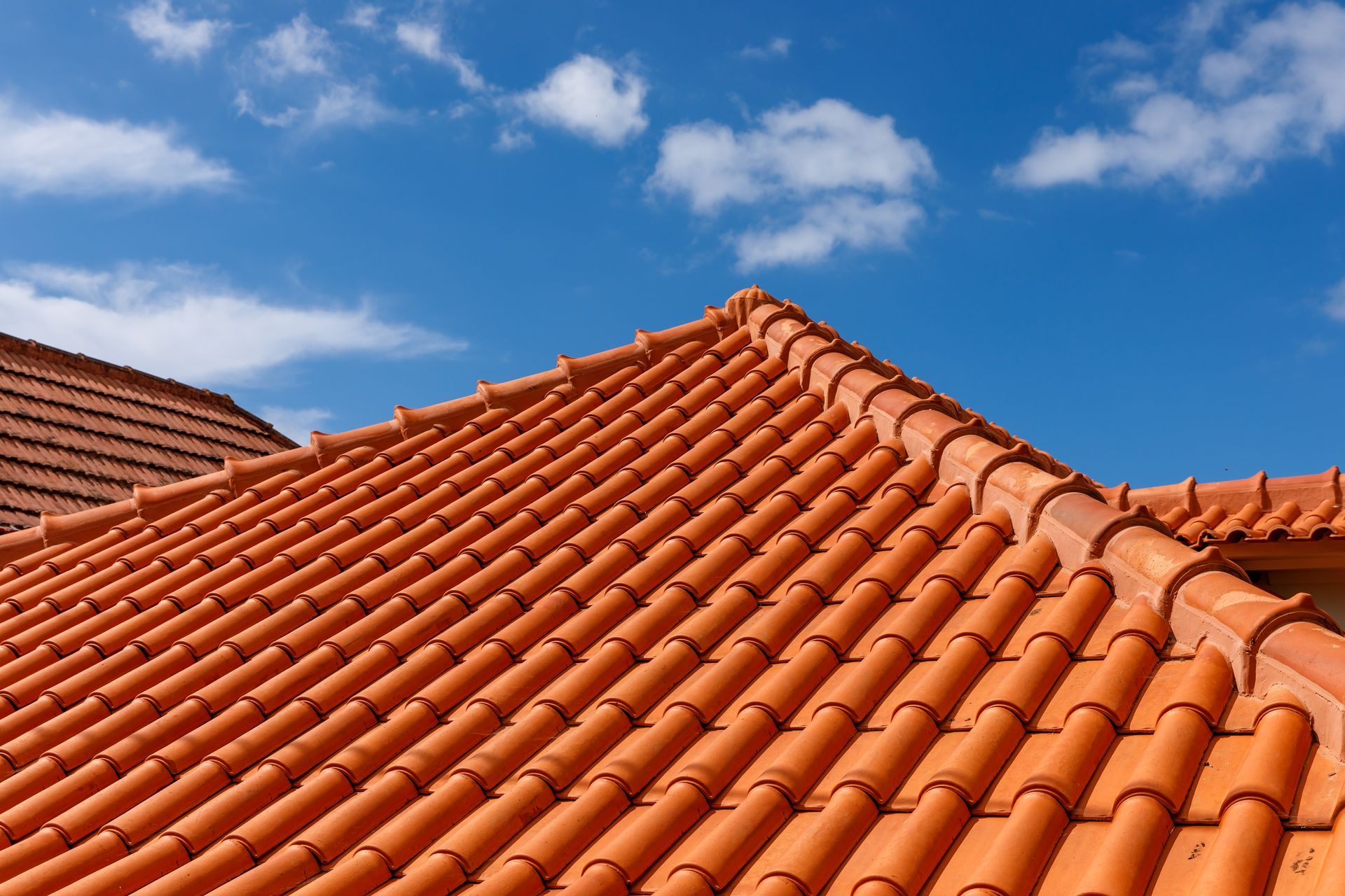 Red clay tile roof against a bright blue sky with wispy clouds.
