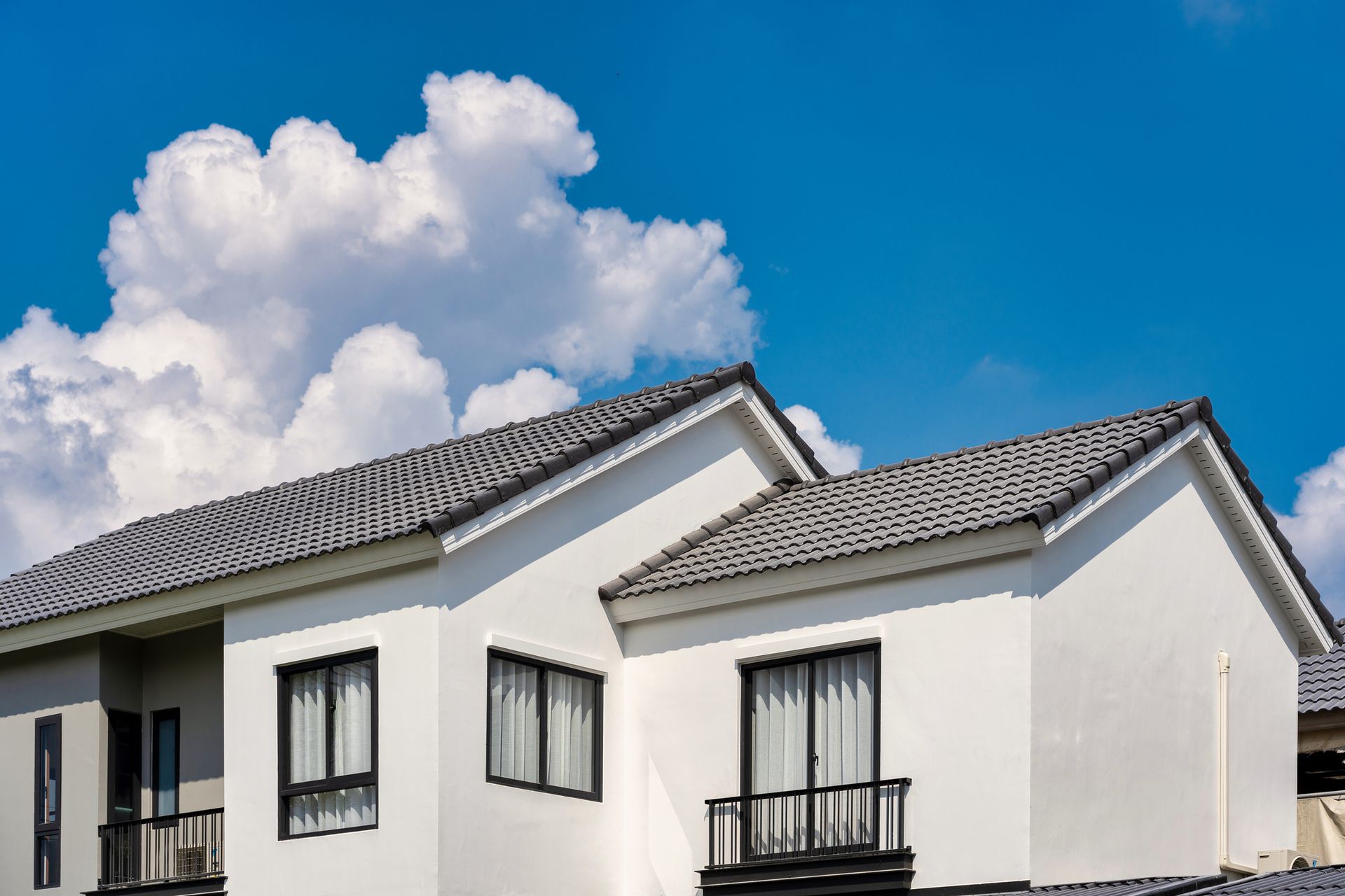 White house with gray roof, black window frames and railings, against a blue sky with white clouds.
