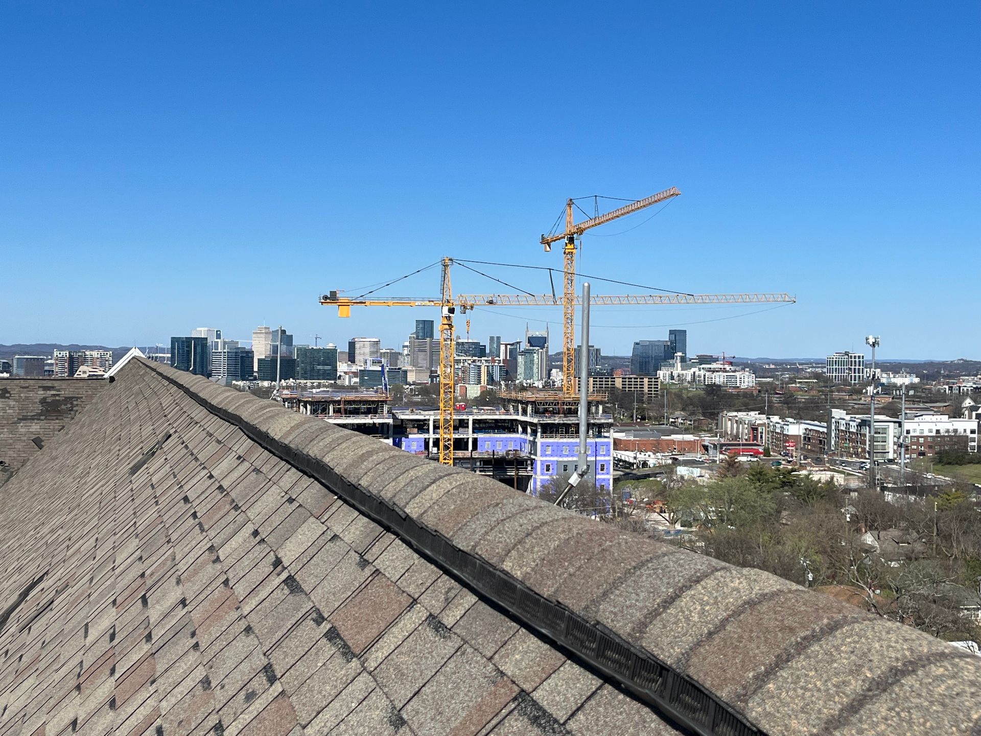 Rooftop view of a city skyline with construction cranes under a clear blue sky.