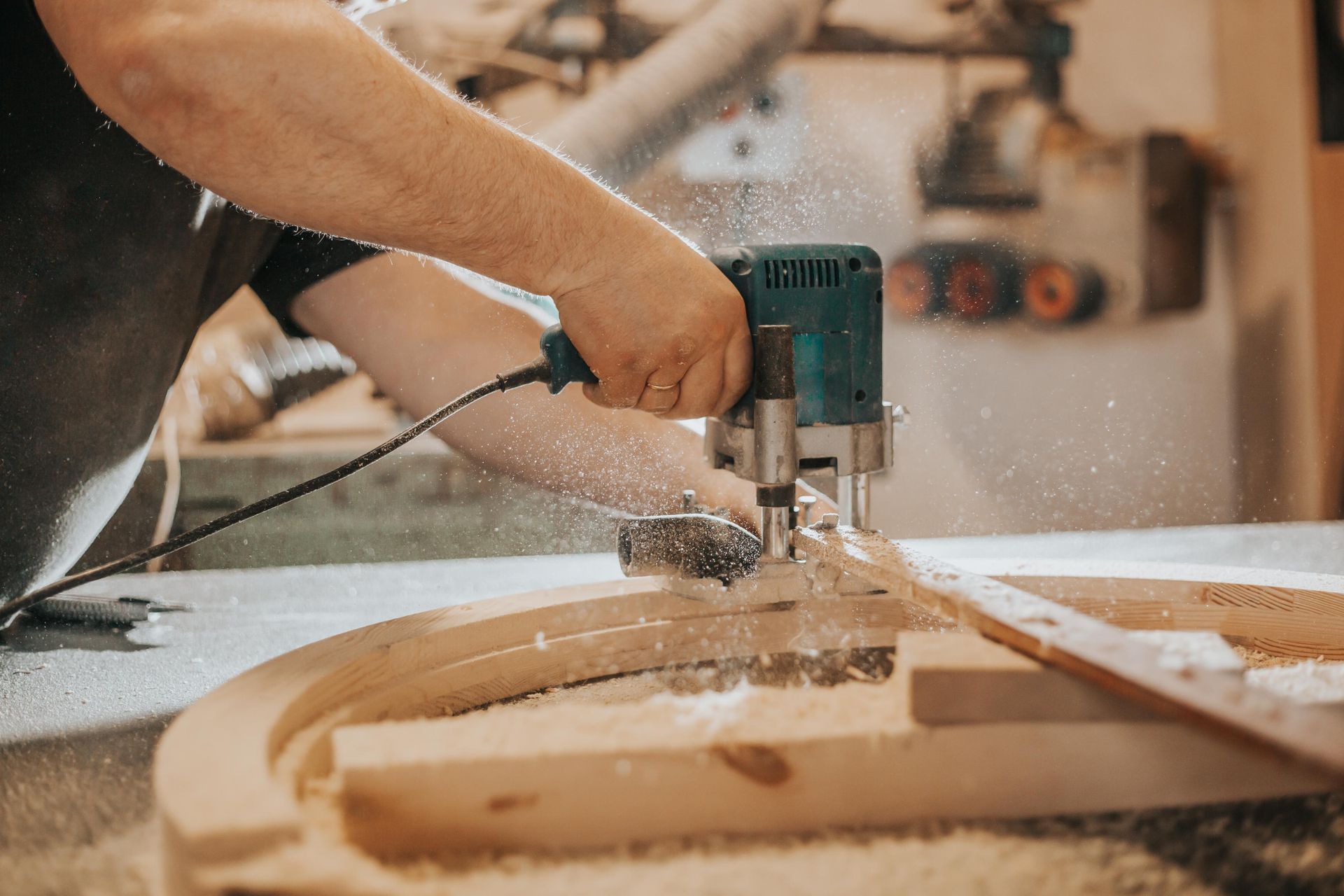 Person using a router on a wooden arch, creating sawdust in a workshop.