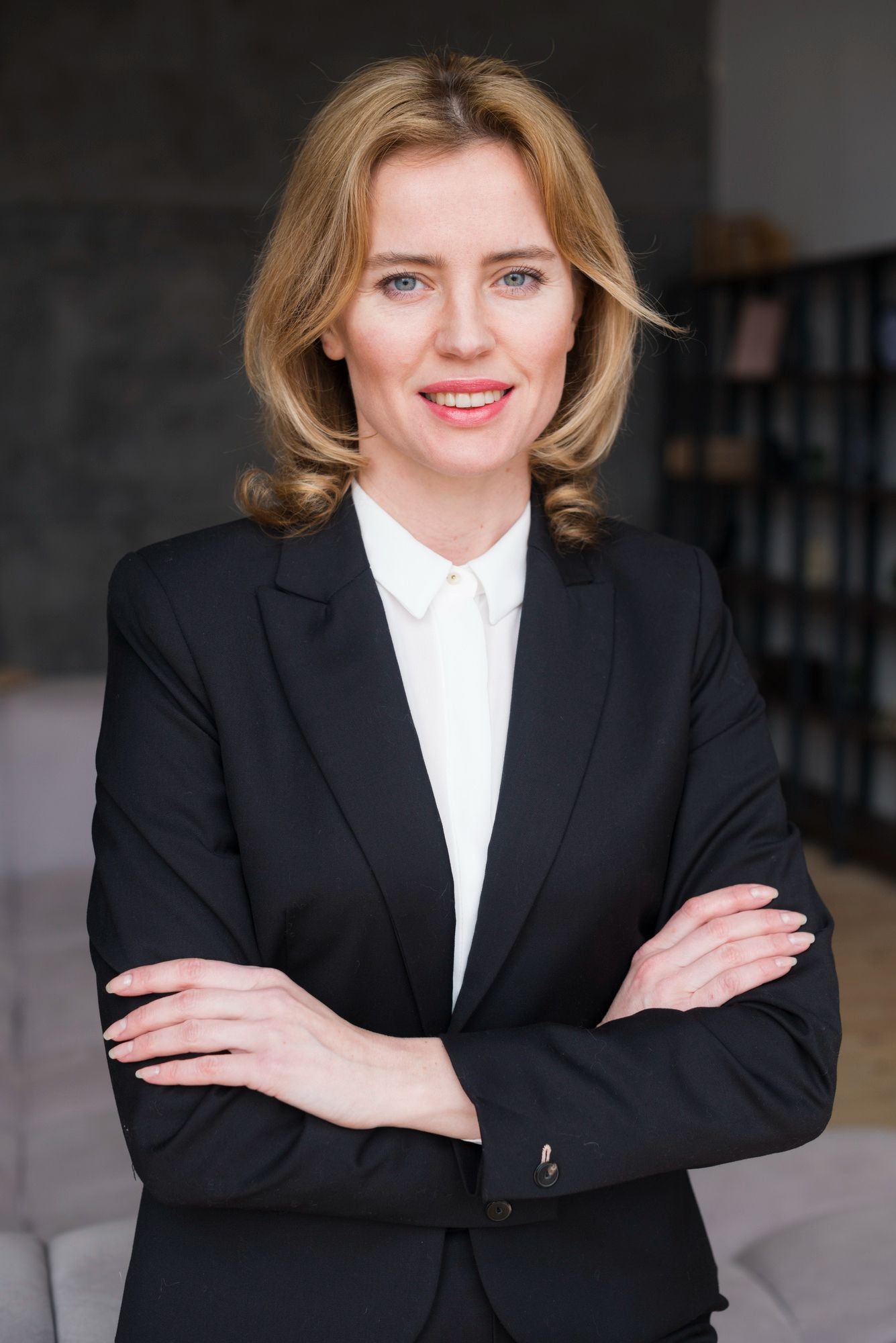 A woman in a black suit and white shirt is standing with her arms crossed.
